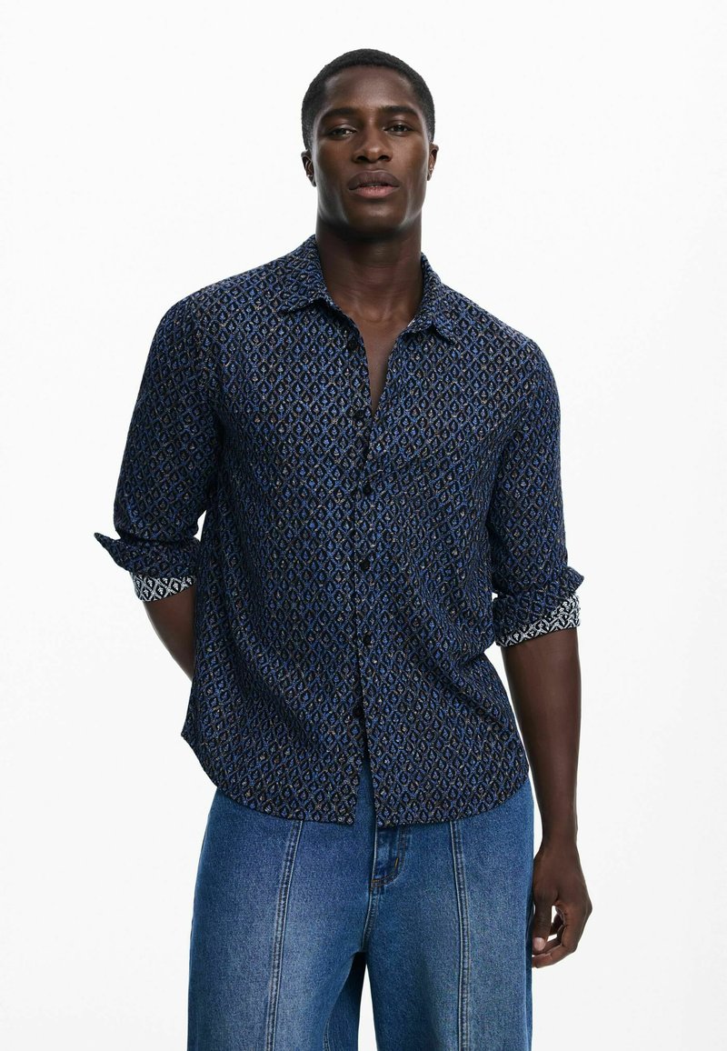 Mėlyna marškiniai su mygtukais ir deimanto raštu, su užlenktomis rankovėmis ir kontrastine apdaila. Dėvimi su šviesiai mėlynomis tiesiomis džinsų kelnėmis.