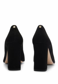 Paire de chaussures à talons hauts en suède noir avec larges talons carrés vues de dos sur un fond blanc.
