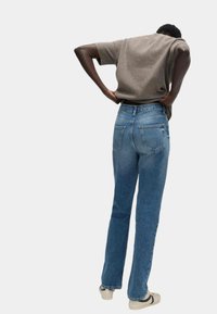 Ciemnoszary krótki top z krótkim rękawem w połączeniu z niebieskimi dżinsami. Dżinsy mają prosty krój nogawek i dwie tylne kieszenie, noszone z beżowymi sneakersami.