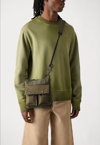 Grønn bomullssweatshirt, avslappet passform. Olivengrønn crossover-veske med to frontlommer og trykknapper, justerbar stropp. Bukser i nøytral farge.