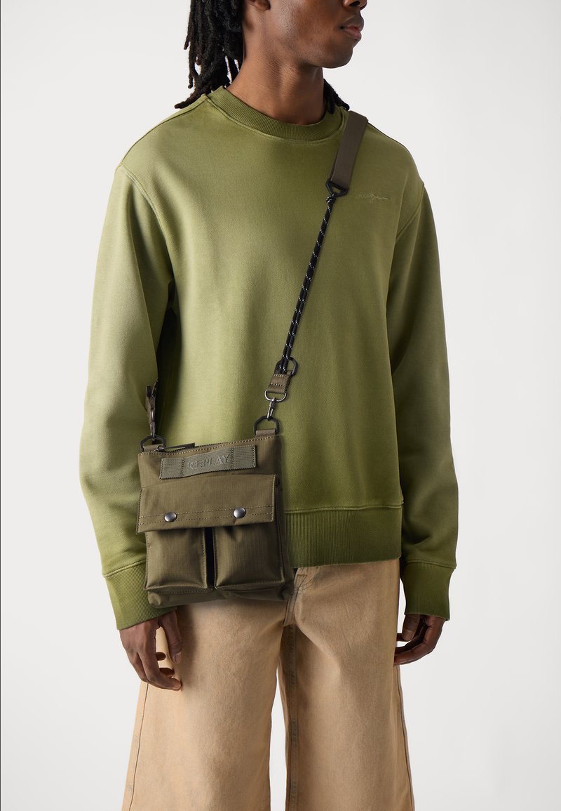 Grønn bomullssweatshirt, avslappet passform. Olivengrønn crossover-veske med to frontlommer og trykknapper, justerbar stropp. Bukser i nøytral farge.