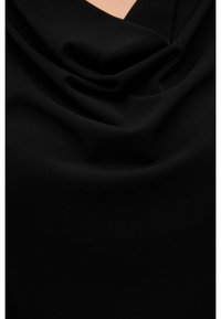 Black fabric draped to create soft folds, showing smooth texture and slight sheen against a neutral background.