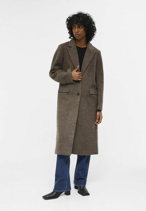 Brown wool blend long coat with a lapel collar, single button closure, two front pockets, worn over black top and blue flared jeans.