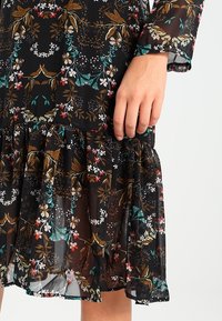 Abito nero con fiori, realizzato in un tessuto leggero e trasparente con intricati motivi di fiori bianchi, rossi, verdi e dorati, e un orlo a balze.
