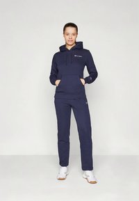 Tmavomodrá fleecová mikina s kapucňou, predným vreckom a sťahovacími šnúrkami, v kombinácii so zodpovedajúcimi teplákmi, oba kúsky s logom na hrudi.