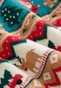 Strickstoff mit festlichem Design, das Rehe, Bäume und geometrische Muster in Rot, Grün, Beige und Creme zeigt. Weiche Textur.