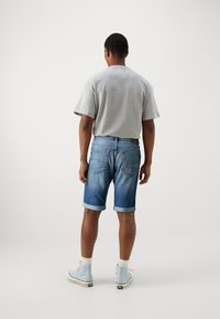 Šedé tričko s krátkým rukávem doplněné modrými denimovými kraťasy s ohrnutými lemy. K outfitu patří tenisky s světle modrými akcenty a bílé ponožky.