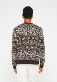 Strickpullover mit einem dunkelbraunen Grundton und weißen geometrischen Mustern, rundem Halsausschnitt sowie gerippten Bündchen und Saum. Weiche Textur, lässige Passform.