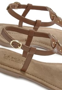 Ruske nahkasaapad strappimallisella suunnittelulla, joissa on kultaiset niittikoristeet ja pehmeä beige mokkanahkainen pohja. Mukana säädettävä solki.