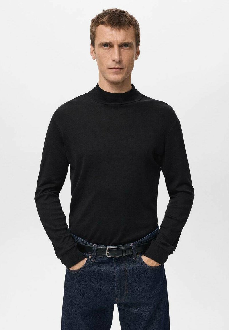 Black long-sleeve turtleneck sweater in a fitted design, made from soft fabric, paired with dark denim jeans and a black belt.