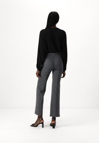 Black long-sleeve top and gray fitted pants with flared legs; model wears black strappy heels. Smooth fabric and tailored fit visible.
