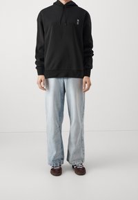 Černá mikina s kapucí a přední kapsou, na které je bílý motiv. Nositelná s volnými světlomodrými džíny a tmavohnědými teniskami.