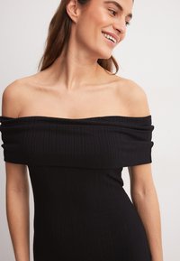 Melns kleita ar atvērtām plecu daļām, ribota tekstūra, pieguļoša siluets, plašs kakla izgriezums un īsas piedurknes.