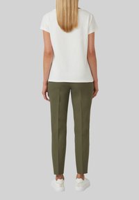 Witte T-shirt met korte mouwen gecombineerd met olijfgroene, op maat gemaakte broek. Glad materiaal, slim fit, en witte sneakers maken de look compleet.