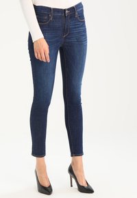 Jeans ajustados de color azul oscuro hechos de denim, con una cintura de altura media y un diseño de cinco bolsillos, combinados con tacones altos negros.