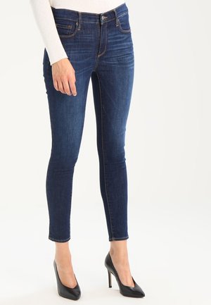 Jeans ajustados de color azul oscuro hechos de denim, con una cintura de altura media y un diseño de cinco bolsillos, combinados con tacones altos negros.