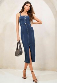 Denim obleka, temno modra, oprijeta z gumbnimi zapiranji spredaj, z naramnicami in stranskim razporkom. Oblečena z sivo torbico in črnimi natikači.