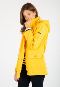 Veste imperméable jaune avec capuche, fermeture éclair à l'avant, poches à boutons-pression et poignets blancs rayés, présentant une texture lisse et brillante.