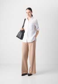 Camicia bianca in lino con un taschino, pantaloni beige a gamba larga, borsa a spalla nera in pelle e scarpe nere con punta affusolata.