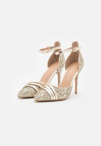 Glittering gold high-heeled shoes with a pointed toe, ankle strap, and horizontal metallic stripes across the front; textured glitter surface.