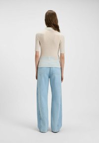 Top a coste di un beige chiaro con maniche corte, abbinato a jeans a gamba larga blu chiaro, visto da dietro. Texture morbida e design casual.