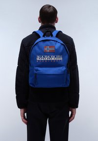 Sac à dos bleu avec un petit écusson de drapeau norvégien et le logo "NAPAPIJRI geographic" en couleurs contrastées. Comprend une poche zippée à l'avant.