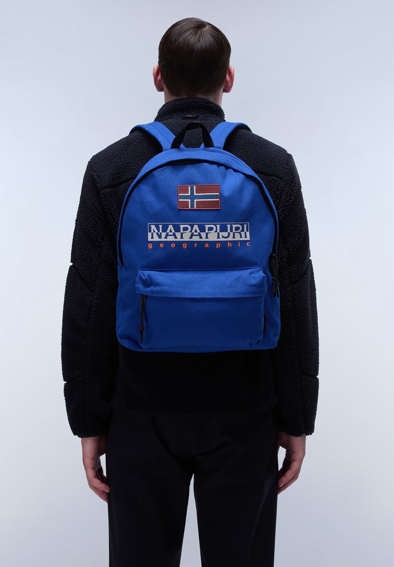 Sac à dos bleu avec un petit écusson de drapeau norvégien et le logo "NAPAPIJRI geographic" en couleurs contrastées. Comprend une poche zippée à l'avant.
