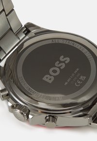 Fond de montre en acier inoxydable avec logo et texte gravés. Présente un boîtier circulaire lisse, une couronne proéminente et une finition métallique brossée.