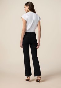 Zwarte wijde jeans gecombineerd met een wit topje met korte mouwen. Het model draagt dierenprint hakken en poseert voor een neutrale achtergrond.