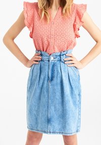 Light pink, short-sleeve, button-up blouse with eyelet pattern. Paired with a high-waisted, blue denim skirt featuring pleats and a belt.