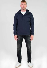 Sudadera marinera con un bolsillo frontal, capucha con cordón y puños de canalé, combinada con jeans de mezclilla oscura y zapatillas blancas.