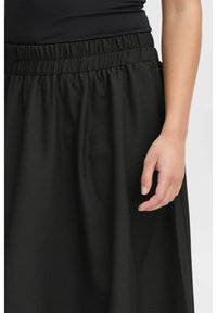 Schwarze, elastische Taillenrock mit glatter Textur, der ein volles Design aufweist. Das Kleidungsstück reicht bis zur Mitte der Wade und betont einen minimalistischen Stil.