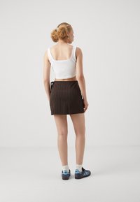 Hvit, avkortet tank topp, brun rutet miniskjørt og blå Adidas-sko med grå såler og hvite ankelstrømper. Minimalistisk design, uformell stil.
