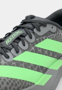 Grey athletic shoe with a snake skin pattern, featuring neon green accent stripes and logo. Lightweight design with textured fabric.