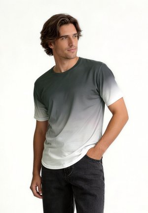 Jeune homme aux cheveux mi-longs portant un t-shirt dégradé du noir au blanc et un jean noir, debout avec une main dans la poche.