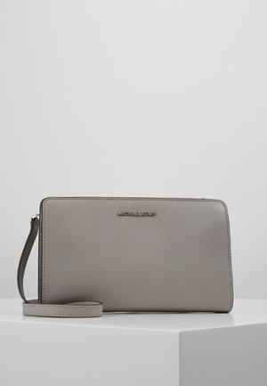 Pochette bracelet Michael Kors grise à surface texturée, fermeture éclair et bracelet amovible, posée sur une surface blanche.