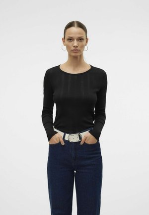 Black long-sleeve top with ribbed texture and crew neckline, paired with high-waisted blue denim jeans and a white belt with a metallic buckle.