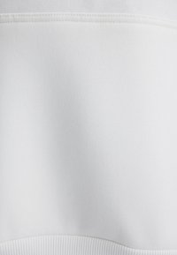 Weißer Sweatshirt-Stoff mit glatter Textur. Verfügt über einen gerippten Saum und saubere Nähte an den Nähten, was ein minimalistisches Design bietet.