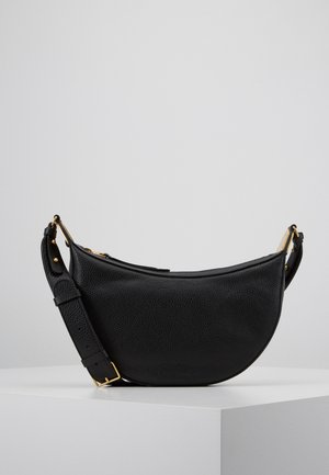 Sac d'épaule en cuir noir en forme de croissant avec bandoulière réglable et garnitures dorées posé sur une surface blanche.