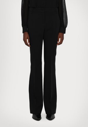 Black flared trousers with a smooth fabric, featuring a tailored waistband and neat creases, paired with pointed black footwear.