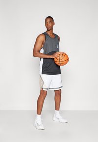 Svart og hvit sporty tank top og shorts, med geometriske mønstre. Modellen holder en basketball, iført hvite sneakers og sokker.