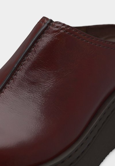 Γυαλιστερό δερμάτινο παπούτσι σκούρου καφέ χρώματος με μαύρη σόλα, που δείχνει λεπτομερείς ραφές κατά μήκος της πάνω άκρης και ομαλό κυρτό σχέδιο.