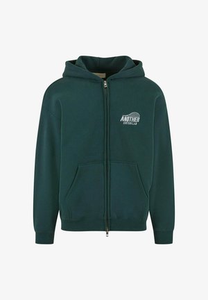 Mørkegrøn zip-up hættetrøje i bomuldsstof, har en lomme foran og hætte, med "ANOTHER COTTON LAB" trykt i hvid på venstre bryst.