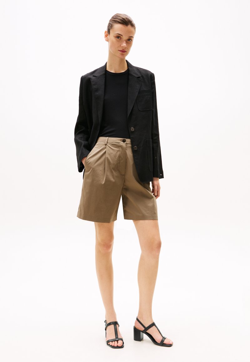 Blazer negro, top negro acanalado, pantalones cortos de khaki con pliegues y sandalias negras de tacón. Tejidos suaves con un corte a medida y acentos mínimos.