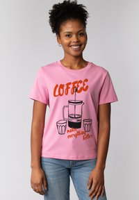 Roze katoenen t-shirt met een afbeelding van een Franse pers, twee kopjes, en de tekst "KOFFIE maakt alles beter" in vet oranje en zwart.