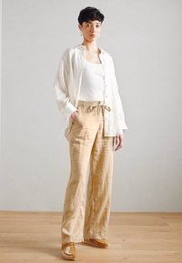 Linen button-up shirt, white tank top, and light beige wide-leg pants with a drawstring. Accented with soft textures and casual loafers.