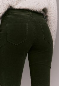 Pantaloni din catifea cord cu un design ajustat, prezentând două buzunare la spate și nervuri verticale subtile pentru textură.