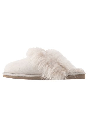 Sabrinha de camurça branca com uma faixa de pelagem felpuda na parte superior. Design de bico arredondado com sola almofadada e fundo texturizado.