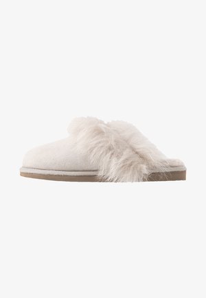 Sabrinha de camurça branca com uma faixa de pelagem felpuda na parte superior. Design de bico arredondado com sola almofadada e fundo texturizado.