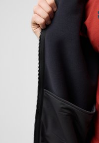 Marineblaue Fleecejacke mit schwarzem Innenfutter, ausgestattet mit einem Reißverschluss und einer großen seitlichen Tasche. Strukturiertes Gewebe für Wärme und Komfort.